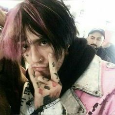 a man with pink hair and piercings on his fingers posing for the camera while another man looks on