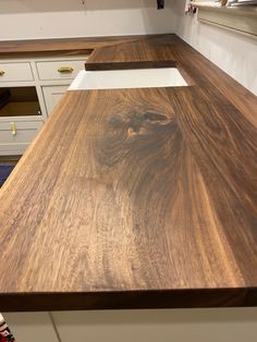 a wooden counter top in a kitchen with white cabinets and drawers on the wall behind it