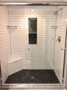 a walk in shower sitting next to a white tiled wall and floor covered in black tile