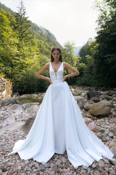 a woman in a white wedding dress standing on rocks next to a river and trees