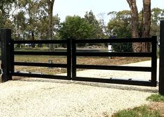 a black gate is in the middle of a gravel area and trees are behind it