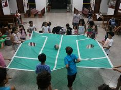 a group of children standing around a giant tennis court with balls on it's surface