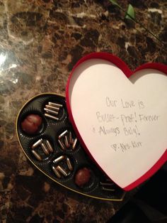 a heart shaped box filled with chocolates on top of a marble countertop next to a note