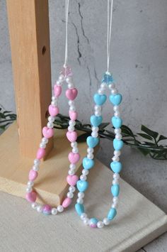 two necklaces made out of beads on a wooden stand with greenery in the background