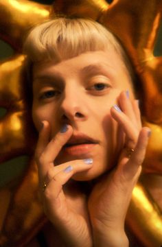 a woman with blue and white nail polish holding her hands to her face in front of gold balloons