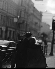 a man and woman standing next to each other on a sidewalk in front of traffic lights