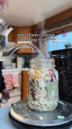 a jar filled with food sitting on top of a counter next to a person pouring something into it