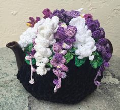 a crocheted tea cosy with flowers on the outside and inside, sitting on top of a rock