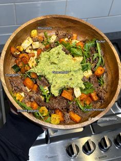 a wooden bowl filled with meat, vegetables and guacamole on top of a stove