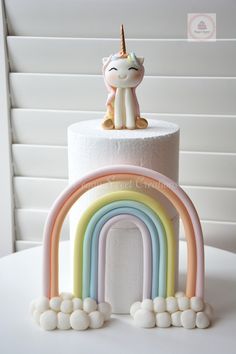 a white cake with a rainbow and a unicorn figurine on top is shown