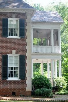 an old brick house with black shutters and white balconies on the second story