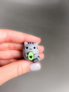 a person holding a tiny toy cat with a green heart on it's nose