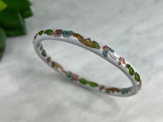 "A vintage cloisonne enamel bangle, featuring pink & blue flowers on a white enamel background, accented with green leaves. Measures about 8\" around on the inside and .25\" wide.  Actual packaging will vary depending on item/s purchased and tape pattern available. Props shown in photos is for display purposes only, not included in this listing. As always, satisfaction is guaranteed. Thanks for shopping Vintage In Bloom! More bracelets: http://www.etsy.com/shop/VintageInBloom?section_id=5488599 Handmade Enamel Bangle, Vintage Enamel Bangle As Gift, Adjustable White Vintage Bangle, Green Enamel Bangle, Vintage Enamel Bangle For Gift, Adjustable Vintage Enamel Bracelets, Vintage Flower-shaped Metal Bracelets, Tape Pattern, Enamel Bangle