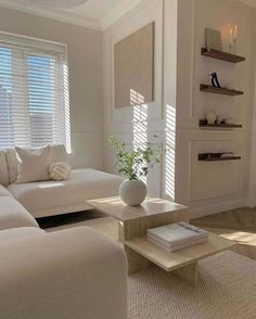 a living room filled with white furniture and windows covered in shades of light shining through the blinds