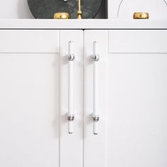 a white cabinet with two gold handles and a clock on the wall in the background