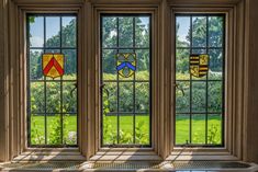 three stained glass windows with emblems on them in front of a green field and trees