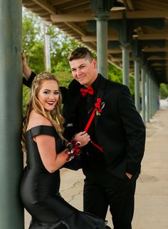 a man standing next to a woman in a black dress and red bow tie on