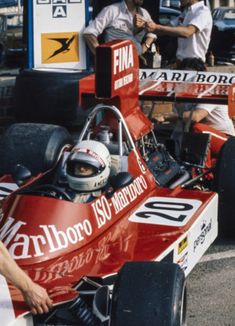 a man sitting in a racing car with other men standing around him and looking at it