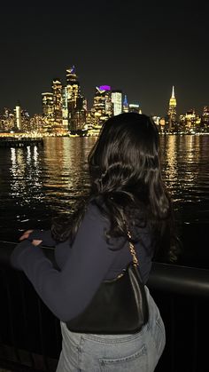 a woman looking at the city skyline from across the water with her purse in hand