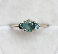 a ring with three stones on it sitting on a white piece of cloth in front of a white background