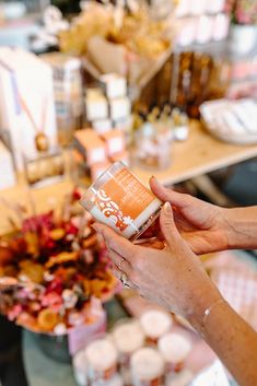 a woman holding up a can of coffee in front of a table full of cupcakes