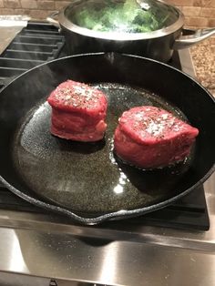 two pieces of steak cooking in a skillet on the stove top next to an oven