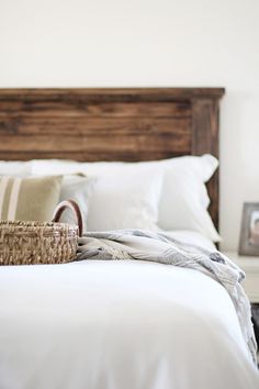 a basket sitting on top of a bed with white sheets and pillows next to a wooden headboard