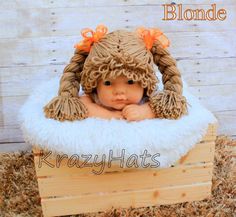 a baby doll in a wooden crate wearing a knitted hat with orange bows on it's head