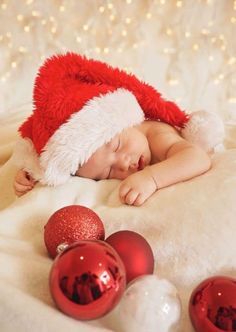 a baby wearing a santa hat sleeping next to christmas ornaments