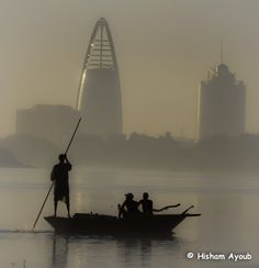 three people in a boat on the water with tall buildings in the backgroud