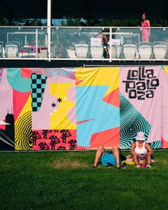 two people sitting on the grass in front of a large banner