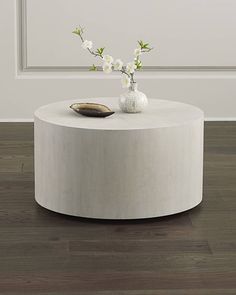 a white round table with flowers on it in front of a wall and wooden floor