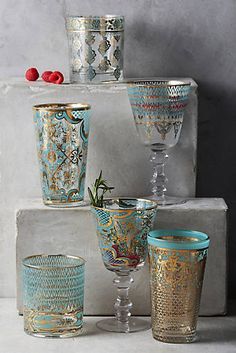 there are many glass vases and cups on the shelf together, one is blue with gold designs