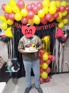 a man standing in front of a birthday cake with balloons on the wall behind him