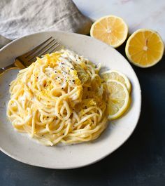 a white plate topped with pasta and lemon wedges