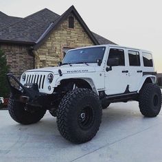 a white jeep is parked in front of a brick house with large tires on it