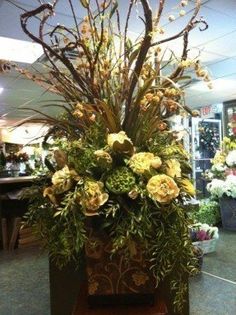 a vase filled with yellow flowers on top of a wooden table next to plants and potted plants