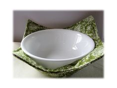 a white bowl sitting on top of a green and white place mat with a napkin underneath it