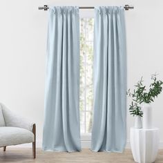 a white chair sitting next to a window covered in blue drapes and a potted plant