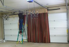 a man standing on a ladder in front of a garage door with curtains hanging from the ceiling