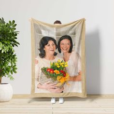 two women holding a bouquet of flowers in front of a wall hanging on the wall