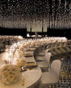 a long table with white chairs and flowers on it is surrounded by chandeliers