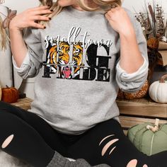 This makes the perfect vintage school spirit tigers sweatshirt! Small Town Big Pride! This tiger sweatshirt is great for the sports moms and tiger lovers! This distressed small town big pride design is perfect on the popular Gildan brand sweatshirt. This vintage style sweatshirt will keep you warm throughout the football season!  A pre-shrunk, classic fit sweater that's made with air-jet spun yarn for a soft feel and reduced pilling. ** P R O D U C T **  - 50% cotton, 50% polyester  - Pre-shrunk  - Classic fit  - Direct to Garment print (no stencils or vinyl which means it will last a lot longer)   - Printed and Shipped in the USA  - Due to different monitor screens colors may vary ** S I Z I N G **  - Consult size chart in listings for measurements  - Sizing is Unisex for all tees, runs t Athletic Heather Fan Apparel Sweatshirt For Fall, School Spirit Sweatshirt With Team Name For Fall, Athletic Heather Sweatshirt With Graphic Print For Fall, College Team Name Sweatshirt For Fall, Fall Fan Gear Tops With Lettering, Collegiate Athletic Heather Sweatshirt For Fall, Athletic Heather College Sweatshirt For Team Spirit, Fall School Spirit Sweatshirt With Lettering, Team-colored Pre-shrunk Sweatshirt For Fall