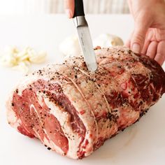 a person cutting meat with a knife on a white counter next to garlic and pepper