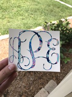 someone holding up a card with the letter b on it in front of some bushes