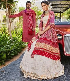 a man and woman standing next to each other in front of an old red car