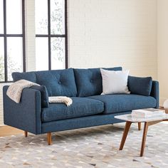 a blue couch sitting in front of a window next to a table with a book on it