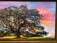 a painting of a large tree in the middle of a field with colorful sky and clouds