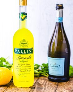 two bottles of wine sitting on top of a wooden table next to lemons and leaves