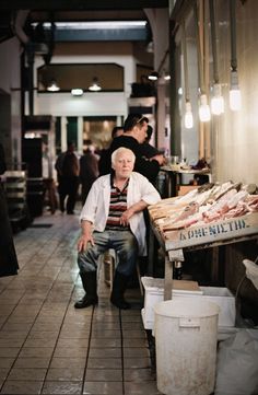 an old man sitting on a bench in front of a fish stand at the market